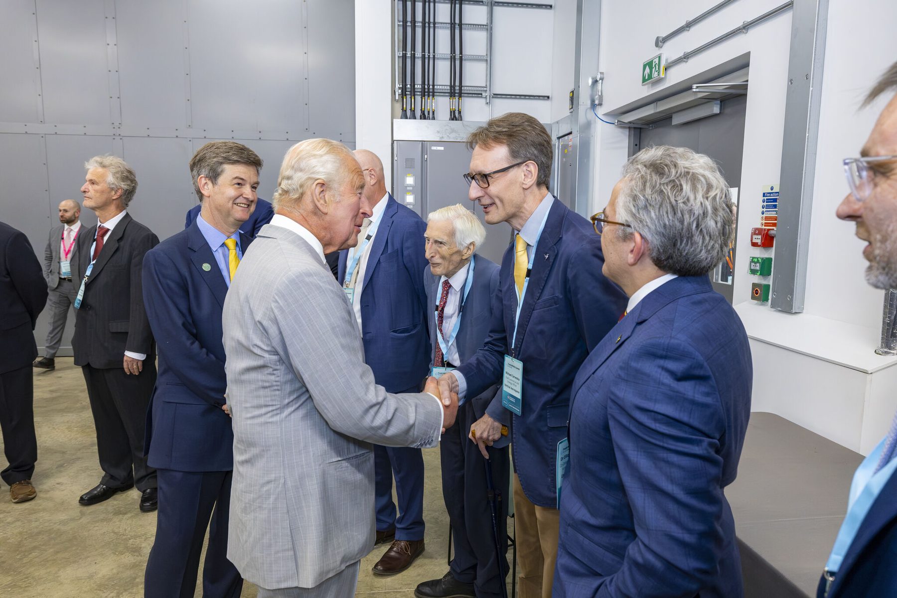 His Majesty King Charles III shaking hands with a guest in the receiving line inside the New Whittle Laboratory, watched by other delegates wearing Frank Whittle Summit lanyards.